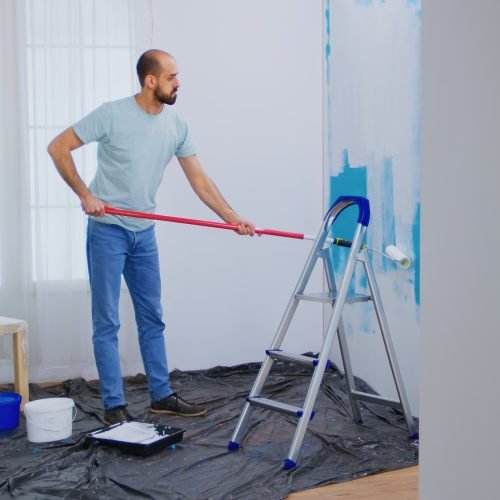 masaking-blue-paint-with-roller-brush-dipped-white-paint-handyman-renovating-apartment-redecoration-home-construction-while-renovating-improving-repair-decorating